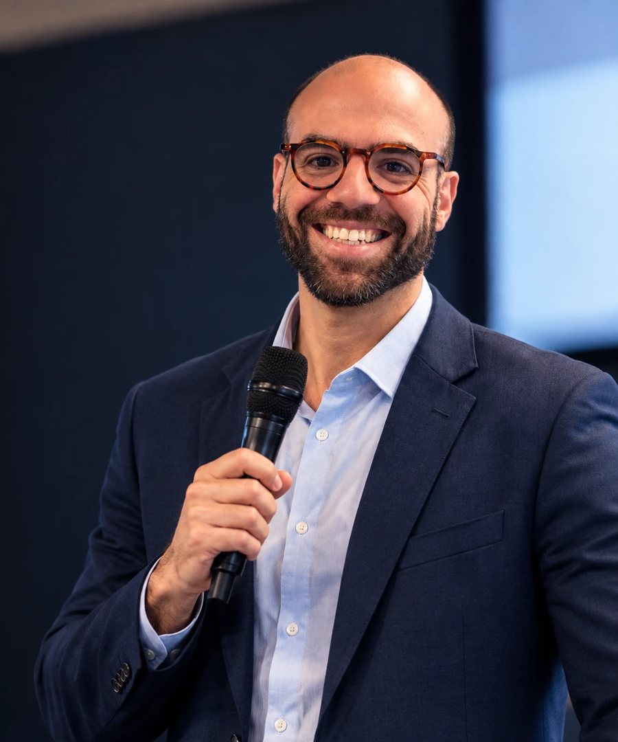 Bernardo Costa sorrindo, com microfone na mão, durante palestra